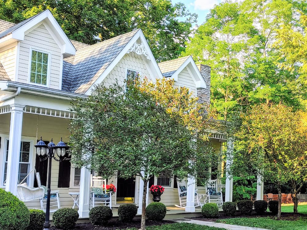 A charming house surrounded by greenery and flower-filled pots on a sunny day.
