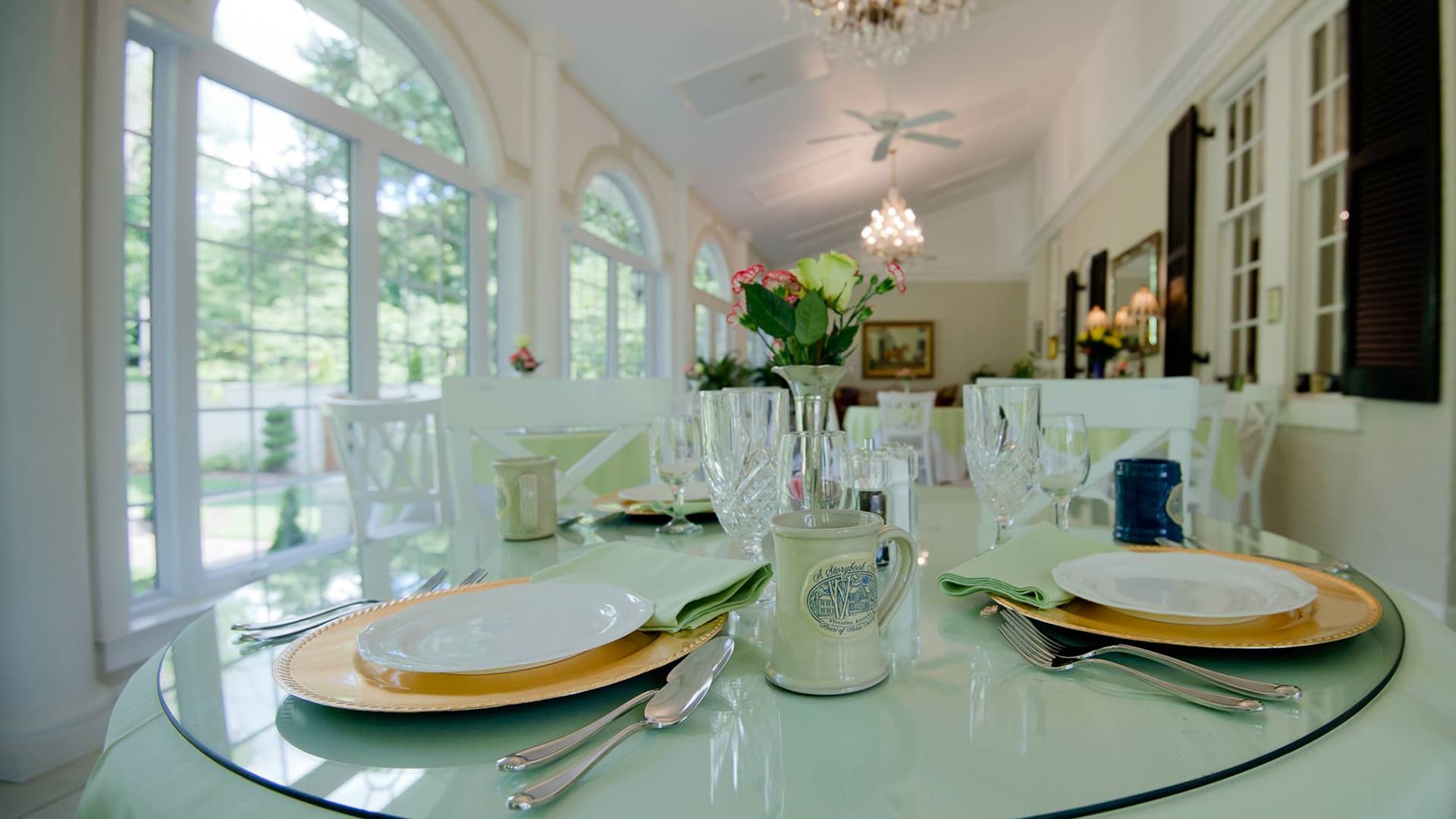 A beautifully set dining table with plates, glasses, and flowers in a bright, airy room.